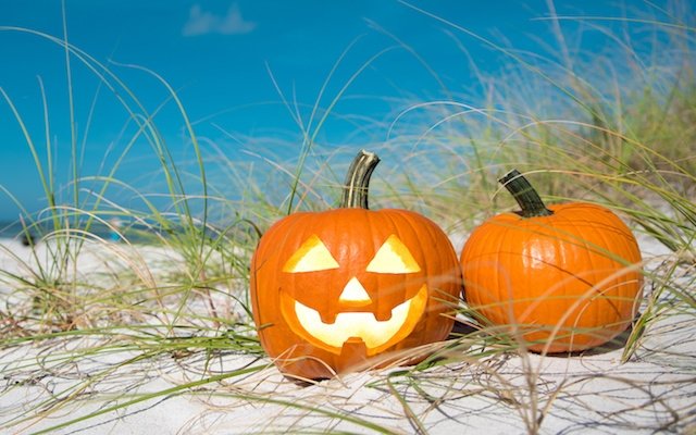 two carved pumpkins sitting in the sand at the beach
