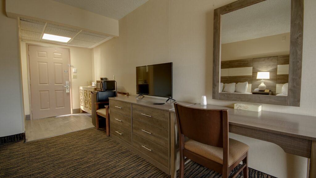 a hotel room with a desk, mirror and television